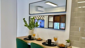 Eine moderne Küche mit Holztresen, zwei grünen Stühlen, einem Blumentopf und einer Frühstücksauslage, darunter Croissants und Orangensaft.