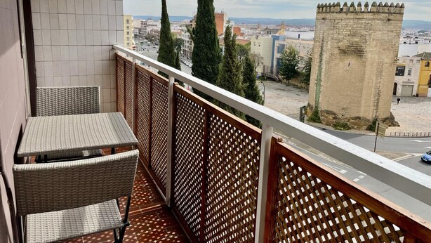 Ein Balkon mit Korbmöbeln, Blick auf eine Stadtlandschaft und ein historischer Turm.