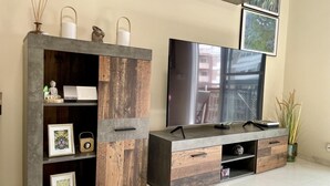 Ein modernes Wohnzimmer mit großem Flachbildfernseher, Holz- und Metallmöbeln und gerahmten Kunstwerken an den Wänden.