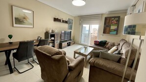 Ein Wohnzimmer mit einer Couch, Sesseln, einem Couchtisch, einem Fernseher und einem Essbereich mit Tisch und Stühlen.