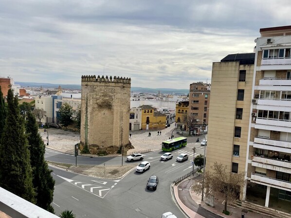 A cityscape with a prominent historical tower, modern buildings, and a busy street with vehicles.