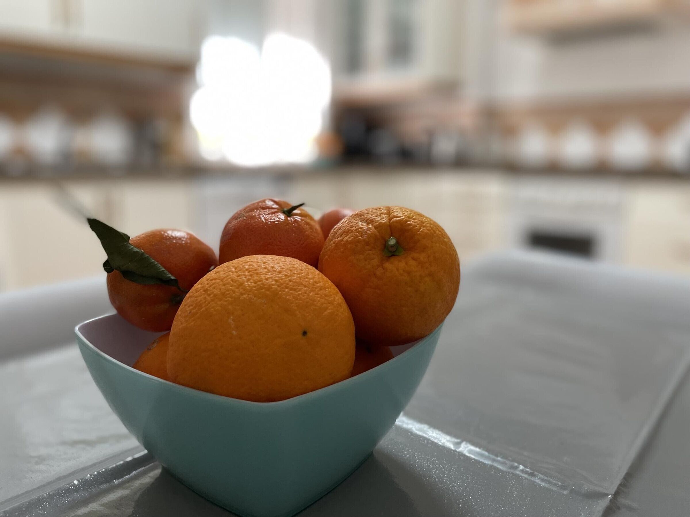 A bowl of oranges on a table with a blurred background.