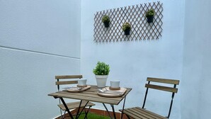 Een klein buiten zitgedeelte met een houten tafel, twee stoelen, een plant in pot en een lattenwand decoratie.