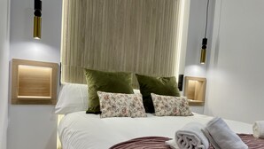 Een moderne hotelkamer met een opgemaakt bed, twee wandlampen en een groot raam met blinds.