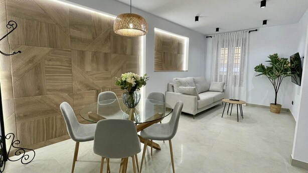 Een moderne woonkamer met een glazen eettafel, grijze stoelen, een witte bank en een potplant.