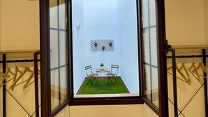 Een kamer met een groot raam, een kleine tafel met stoelen en een hangplant aan de muur.