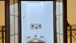 Een klein balkon met een tafel, twee stoelen, een bloempot en een decoratief wandpaneel.