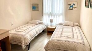 A bedroom with two single beds, a bedside table with a lamp, a window with sheer curtains, and a wall-mounted shelf. - Charming Apartment with Pool & Garage in Córdoba's Prime Shopping District (Córdoba)