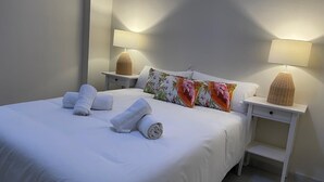 A neatly made bed with rolled towels, a floral pillow, and two bedside lamps on white nightstands. - Casa Terraza Judería: Spacious History-Filled Retreat with Private Terrace in Córdoba's Jewish Quarter (Córdoba)