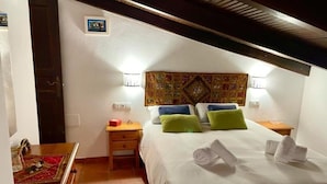 Ein Schlafzimmer mit einem Bett, zwei Nachttischen, einem kleinen Tisch, einem Holzstuhl, einer Wandstickerei und einer Tür.