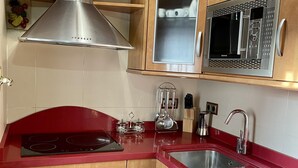 Cozinha com coifa de aço inoxidável, micro-ondas e bancada vermelha.