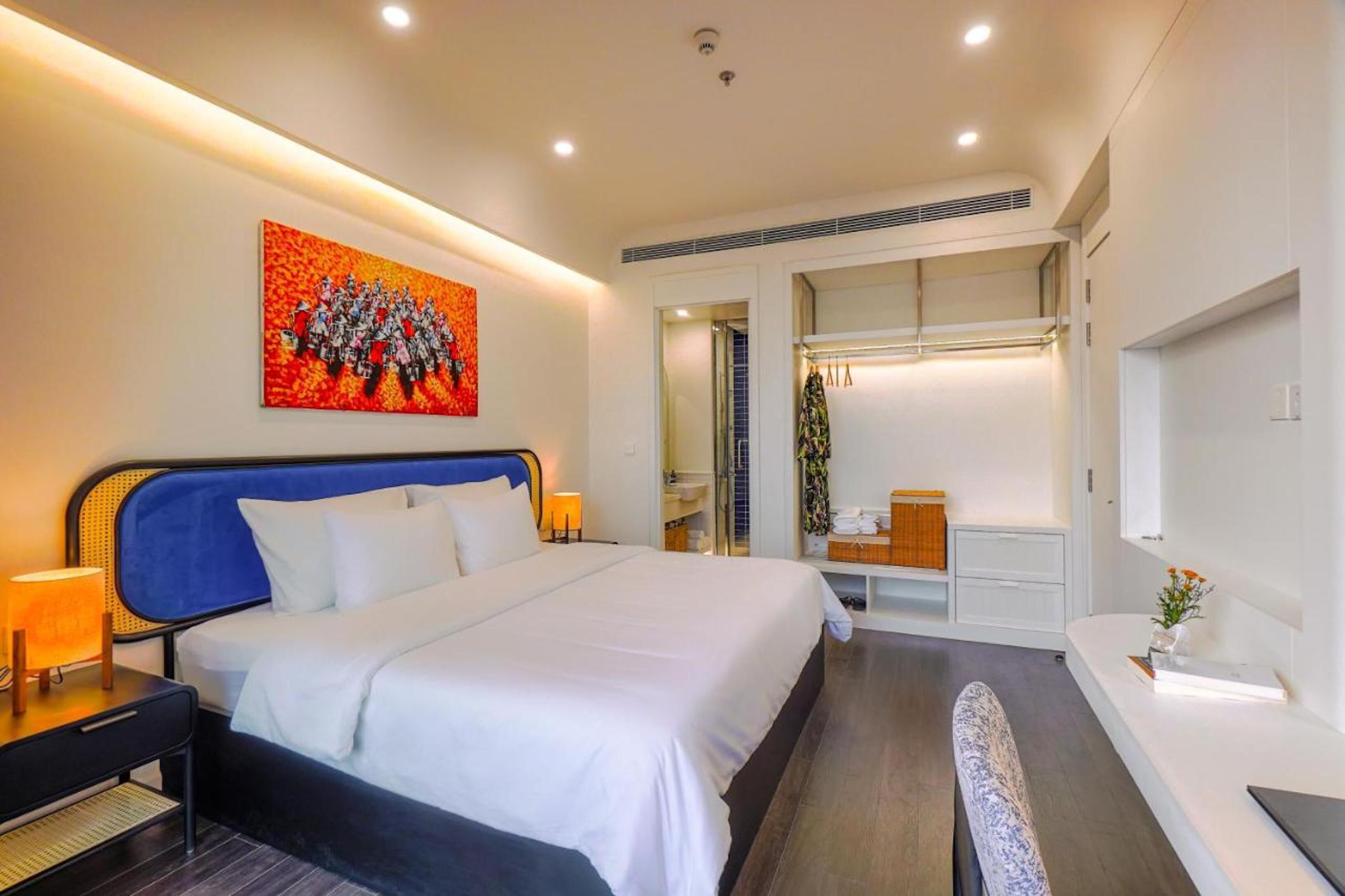 Habitación de hotel moderna con una cama grande, un escritorio, una silla y un baño visible a través de una puerta abierta.