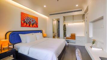 Habitación de hotel moderna con una cama grande, un escritorio, una silla y un baño visible a través de una puerta abierta.