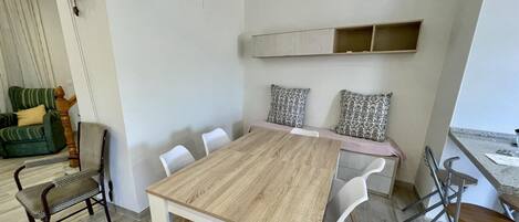 A modern dining area with a wooden table, white chairs, and a bench with patterned cushions.