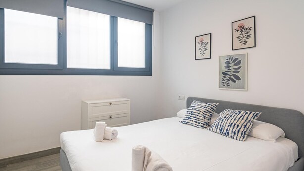 Une chambre à coucher avec un lit, deux oreillers, une table de chevet, une fenêtre et des œuvres d’art murales.