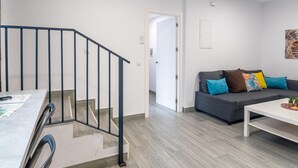 Un salon moderne avec un escalier, un canapé gris agrémenté de coussins colorés et une table basse blanche.