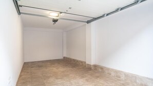 Une pièce dotée d’un sol carrelé, de murs blancs et d’un plafond avec des poutres apparentes et un luminaire.