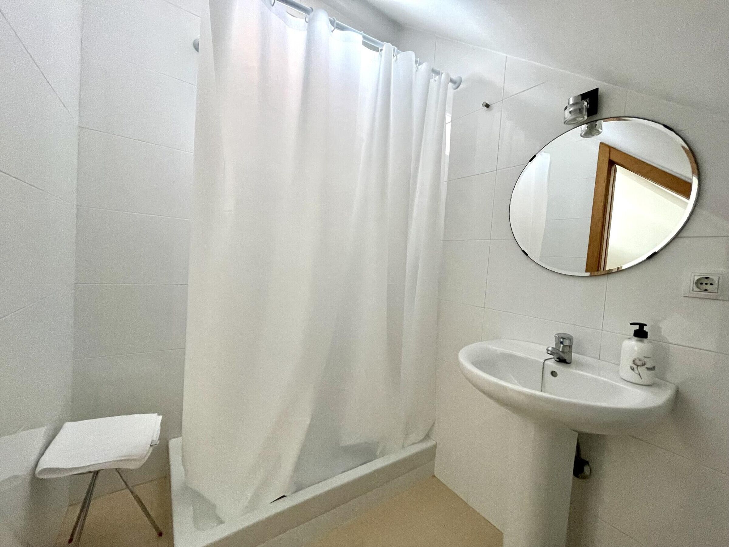 A bathroom with a shower curtain, a sink, a mirror, and a towel stand.
