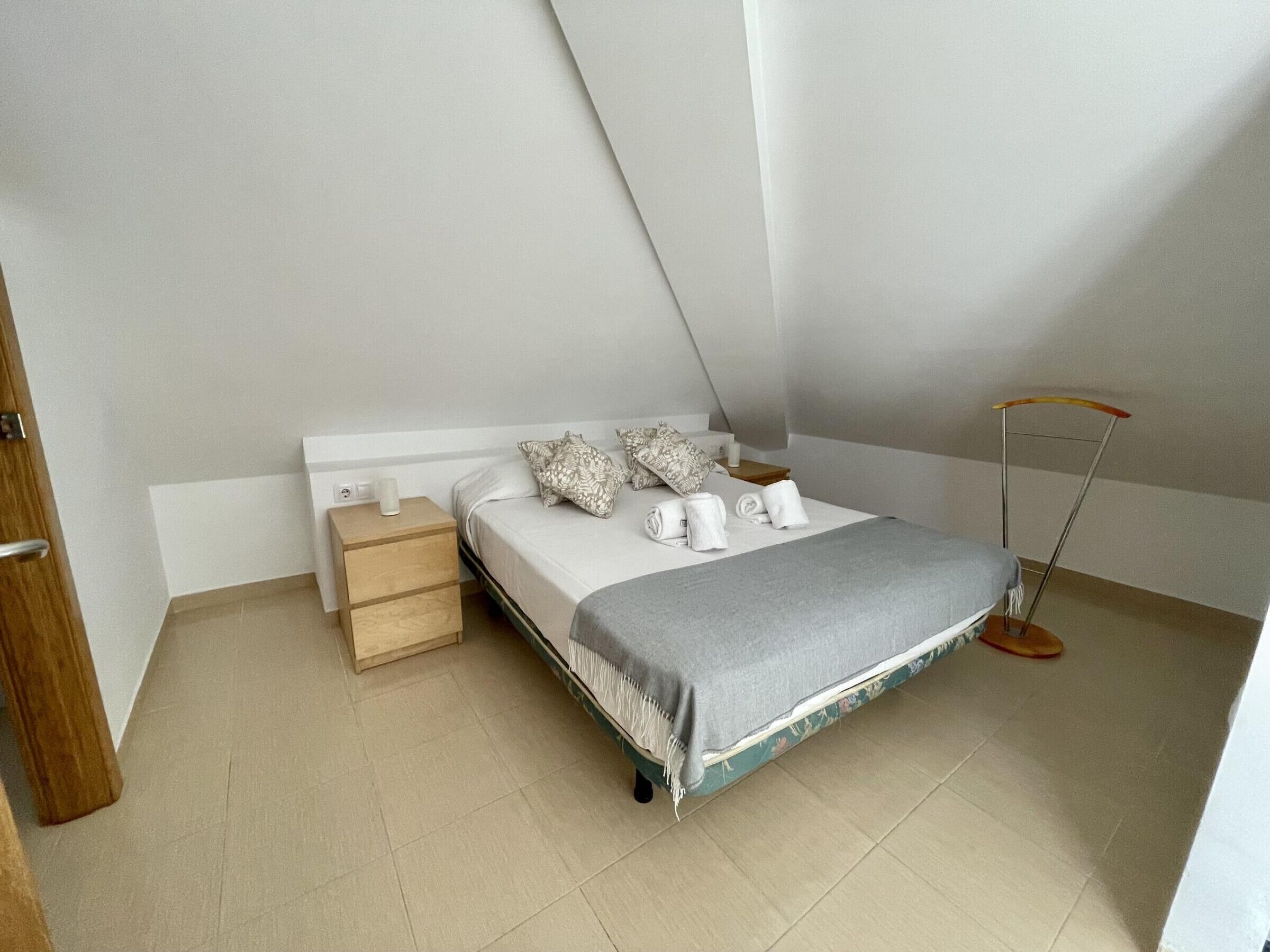 Un dormitorio pequeño y ordenado con una cama individual, una mesita de noche y una lámpara de pie.