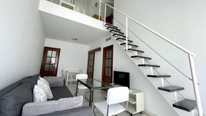 Ein zeitgemäßer Wohnraum mit grauem Sofa, weißem Sessel, Glastisch und einer Treppe mit Glasgeländer.