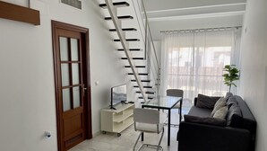Ein modernes Wohnzimmer mit Treppe, Sofa, Sessel und Fernseher auf einem Schrank.