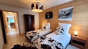 A bedroom with two beds, wooden walls, a cowhide rug, and a ceiling light fixture.
