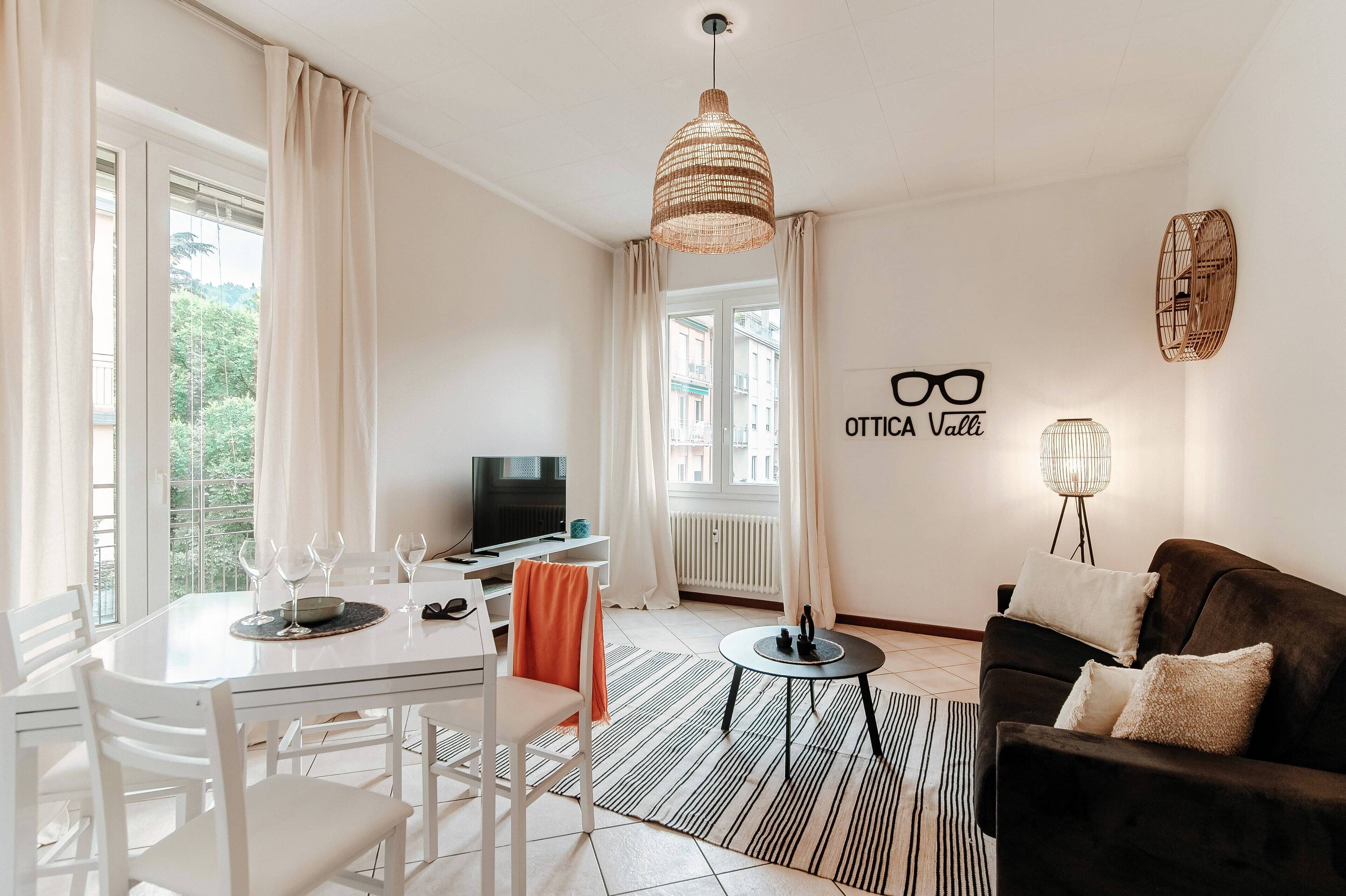 Un salon moderne comprenant un coin repas, un canapé noir, un téléviseur et une grande fenêtre avec des rideaux.