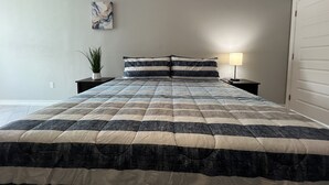 Un dormitorio con una cama grande, dos mesitas de noche, una lámpara de pared y una planta en maceta.