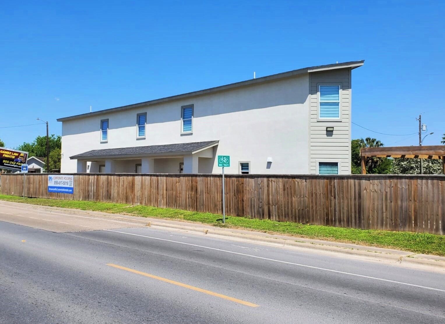 A two-story building with a flat roof, a wooden fence, and a street in front.