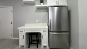 Una cocina con armarios blancos, un refrigerador de acero inoxidable, una encimera y una pequeña planta en un estante.