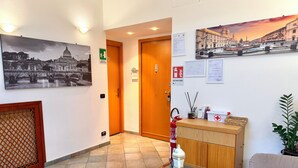 Un hall d’hôtel comprenant un comptoir d’accueil, une table en verre, un canapé et un extincteur.