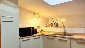 Une cuisine moderne avec des meubles blancs, un puits de lumière, un four à micro-ondes, un évier et un plan de travail sur lequel sont disposés divers objets.