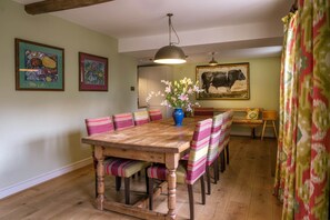 A dining area with a wooden table, striped chairs, a vase of flowers, and a cow painting on the wall. - Idyllic country detached cottage sleeping 8 guests with access to an award winning wellbeing resort (Yorkshire Dales)