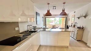 Ett modernt kök med en central köksö, hängande lampor och utsikt över en uteplats.