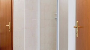 Une porte en bois avec une poignée dorée, qui donne sur une pièce dont les murs sont recouverts de carreaux blancs.