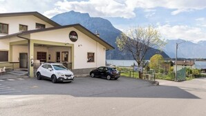 Un bâtiment avec une enseigne indiquant « LA BRASA », situé devant une montagne et un lac. Deux voitures sont garées devant.