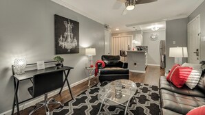 Ein modernes Wohnzimmer mit einer schwarzen Ledersofa, einem Glastisch und einer Chandelüster. Es gibt einen Essbereich mit einem schwarzen Tisch und Stühlen, und eine Küche im Hintergrund.