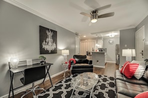 A modern living room with a black leather sofa, a glass coffee table, and a chandelier. There is a dining area with a black table and chairs, and a kitchen in the background. - I48-1 - Apt|Patio|11mi to Convention Ctr|Sleeps 2 (Irving)