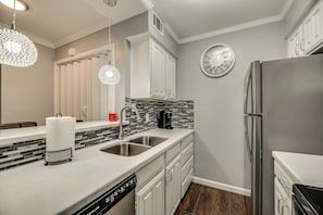 A modern kitchen with white cabinetry, a stainless steel refrigerator, a coffee maker, and a clock on the wall. - I48-1 - Private Irving 1BD |DFW 10 Min | Yard+Pool (Irving)
