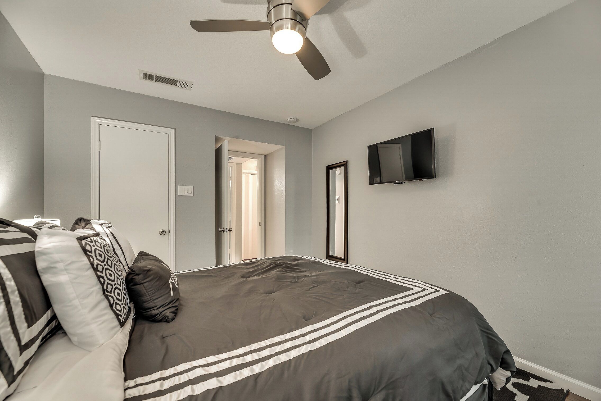 Une chambre à coucher comprenant un lit, un ventilateur de plafond, un téléviseur et une porte donnant sur une autre pièce.