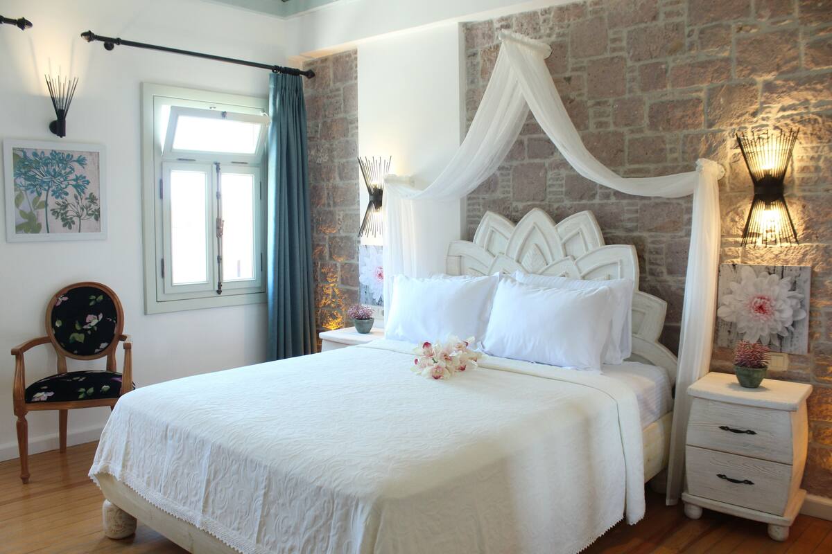 A neatly arranged bedroom with a large bed, a chair, a bedside table, and a wall-mounted lamp.