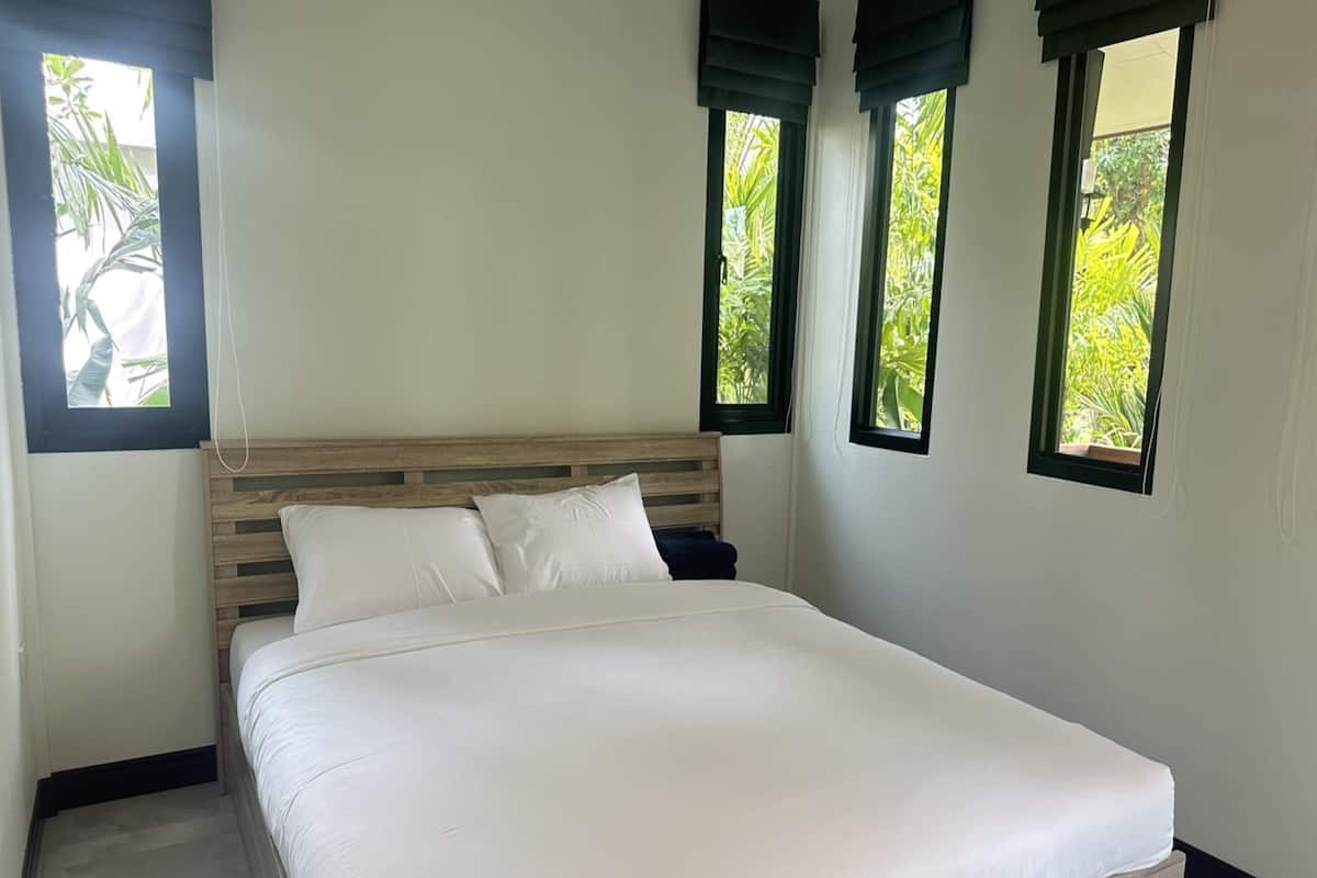 A bedroom with a large bed, a wooden headboard, and three windows with dark blinds.