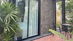 A modern building with a large sliding glass door, a small patio with a table and chairs, and surrounding greenery. - BannRai Tayai Cafe and Resort (Pattaya)