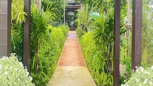A covered pathway flanked by lush greenery and a building in the background. - BannRai Tayai Cafe and Resort (Pattaya)