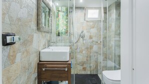 Ein Badezimmer mit Steinwand, Duschkabine aus Glas, Waschbecken in Weiß und Toilette.