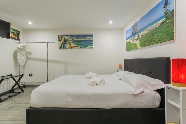 A neatly made bed with white linens and rolled towels, a black headboard, and a red lamp on a bedside table.