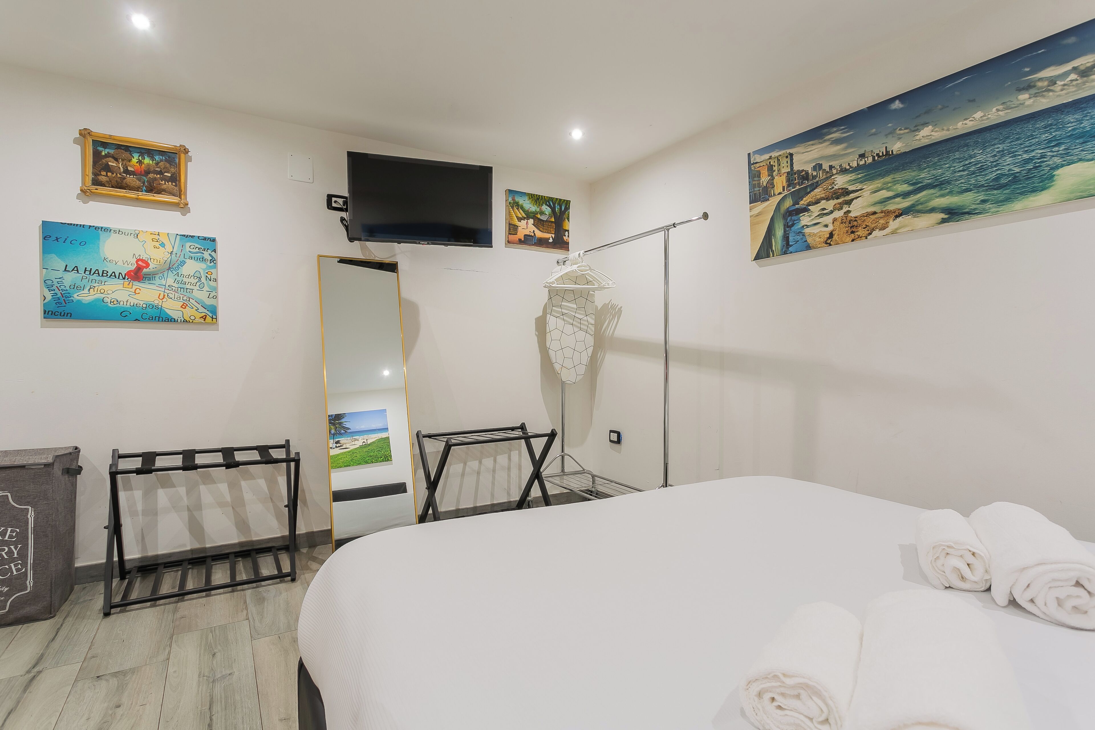 A hotel room with a bed, a TV mounted on the wall, and a painting of a coastal scene.