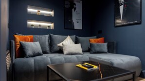 Un salon moderne avec un canapé d’angle gris, une table basse noire et des étagères murales ornées de petites plantes.