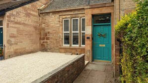 Un bâtiment en pierre avec une porte de couleur turquoise portant l’inscription « Bath Place », une fenêtre avec des volets et une allée gravillonnée devant.