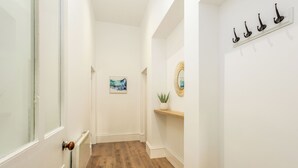 Un couloir avec un plancher en bois, des murs blancs, un radiateur, un tableau, un miroir et un porte-manteau.